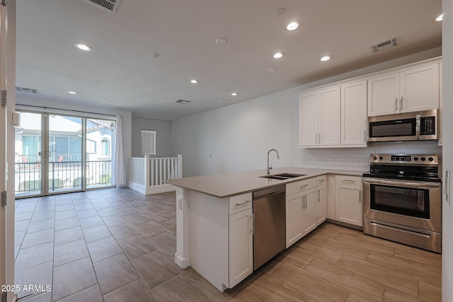 kitchen with appliances with stainless steel finishes, sink, white cabinets, and kitchen peninsula