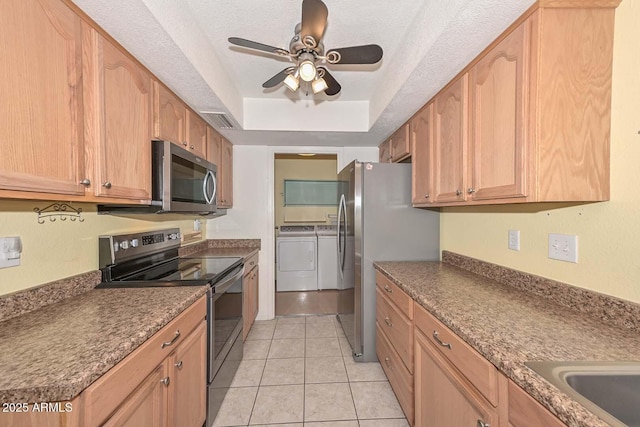 kitchen with light tile patterned floors, a raised ceiling, appliances with stainless steel finishes, a textured ceiling, and separate washer and dryer