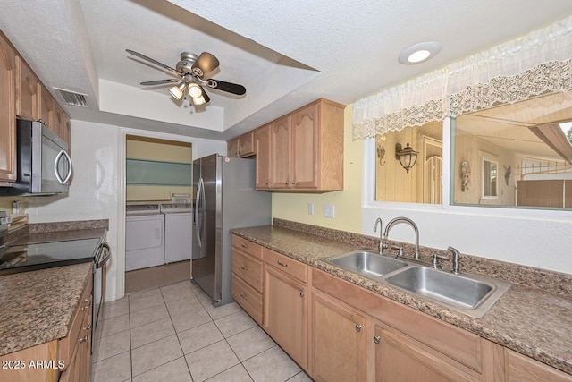 kitchen with visible vents, a raised ceiling, washing machine and clothes dryer, stainless steel appliances, and a sink