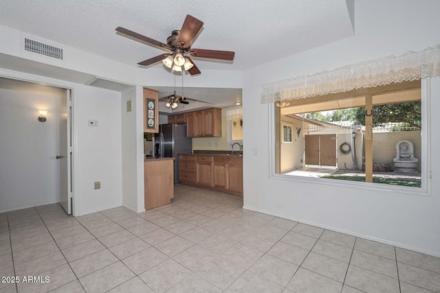 kitchen featuring visible vents, dark countertops, brown cabinets, a textured ceiling, and black fridge