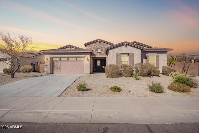 view of front of house with driveway, stone siding, a tiled roof, an attached garage, and stucco siding