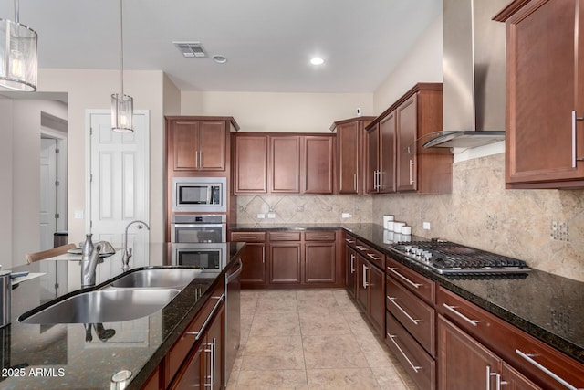 kitchen with visible vents, decorative backsplash, appliances with stainless steel finishes, wall chimney range hood, and a sink