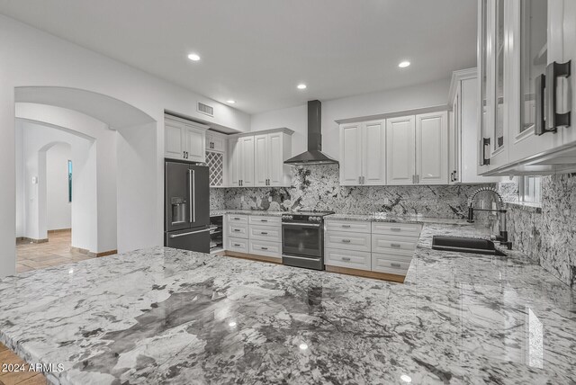 kitchen with wall chimney range hood, appliances with stainless steel finishes, sink, kitchen peninsula, and light stone counters