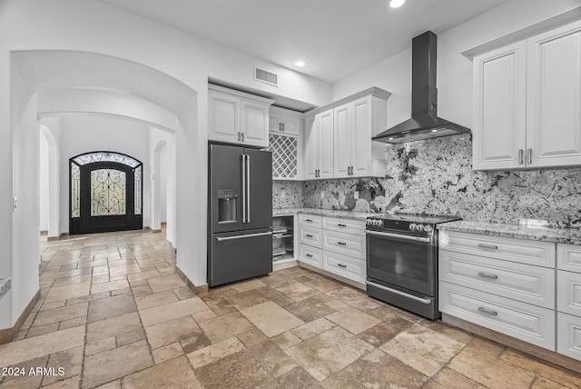 kitchen featuring white cabinetry, wall chimney range hood, stainless steel appliances, and backsplash