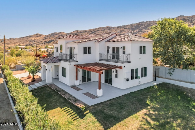 rear view of property with a patio, a mountain view, a balcony, and a yard