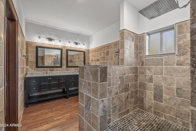 bathroom featuring vanity, a tile shower, wood-type flooring, and tile walls