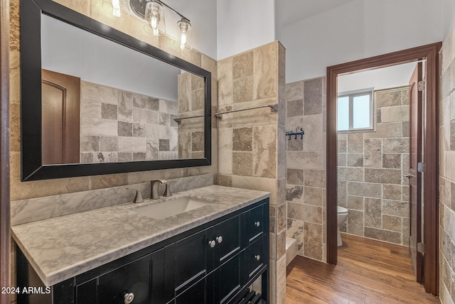 bathroom with a tile shower, hardwood / wood-style floors, toilet, tile walls, and vanity