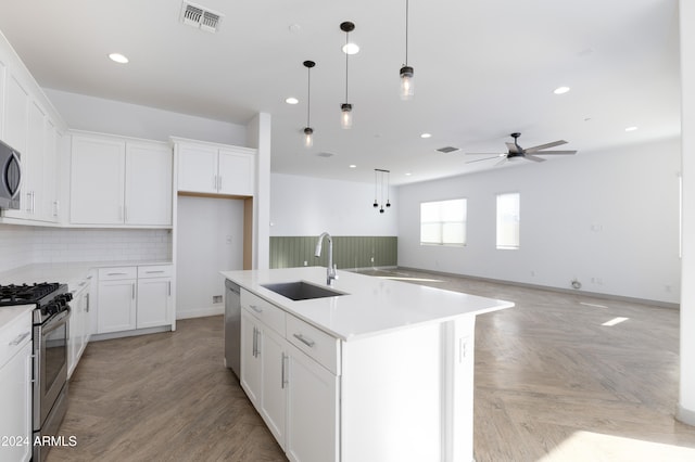 kitchen with ceiling fan, sink, appliances with stainless steel finishes, an island with sink, and white cabinets