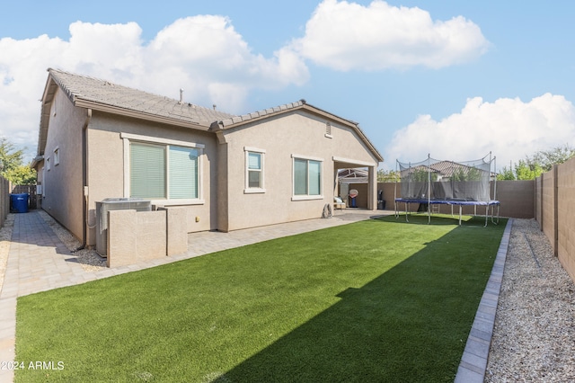 rear view of house featuring a patio area, a yard, and a trampoline