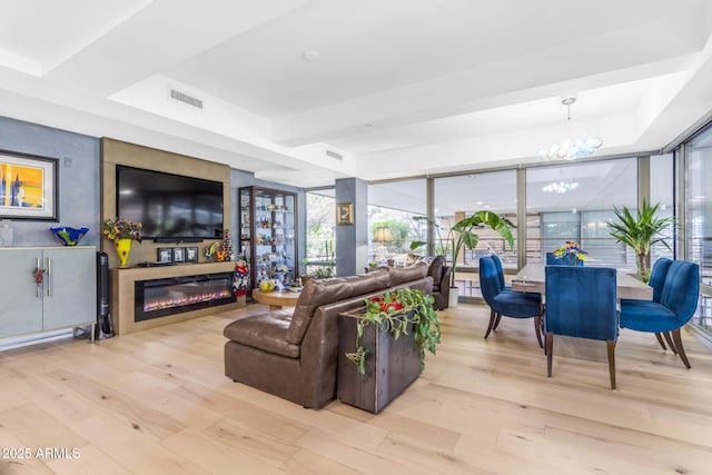 living room with floor to ceiling windows, light hardwood / wood-style floors, a tray ceiling, and a notable chandelier