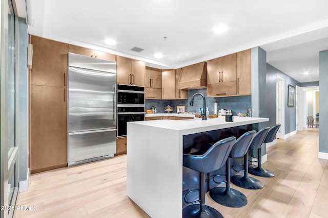 kitchen featuring premium range hood, a kitchen breakfast bar, sink, double oven, and stainless steel built in refrigerator