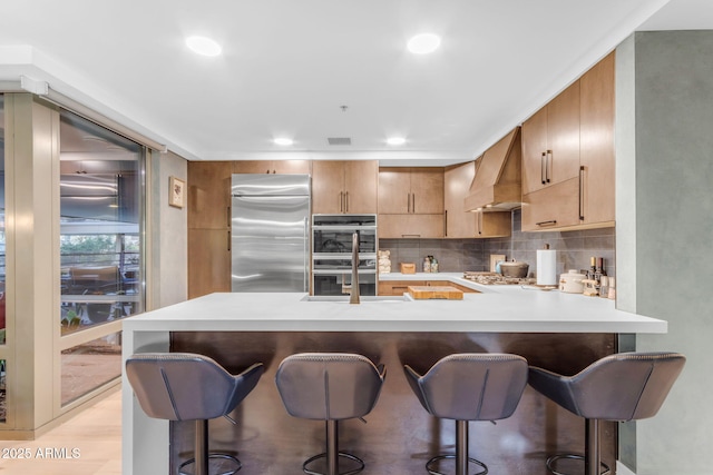 kitchen featuring kitchen peninsula, appliances with stainless steel finishes, a kitchen breakfast bar, custom exhaust hood, and sink