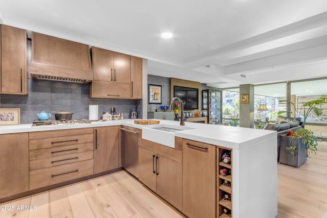 kitchen with sink, decorative backsplash, light wood-type flooring, kitchen peninsula, and stainless steel gas cooktop