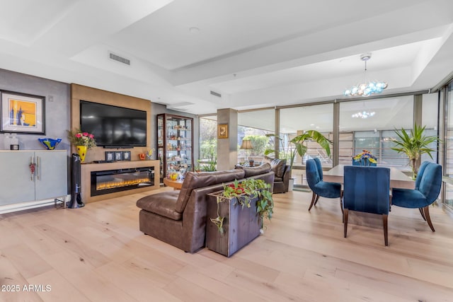 living room with light hardwood / wood-style flooring, a tray ceiling, a notable chandelier, a large fireplace, and a wall of windows