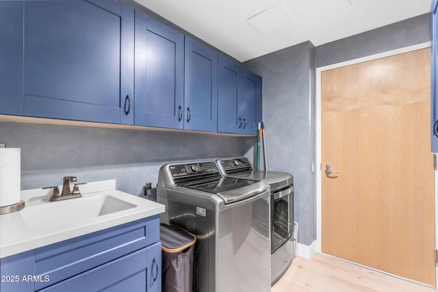 clothes washing area with cabinets, separate washer and dryer, light hardwood / wood-style floors, and sink