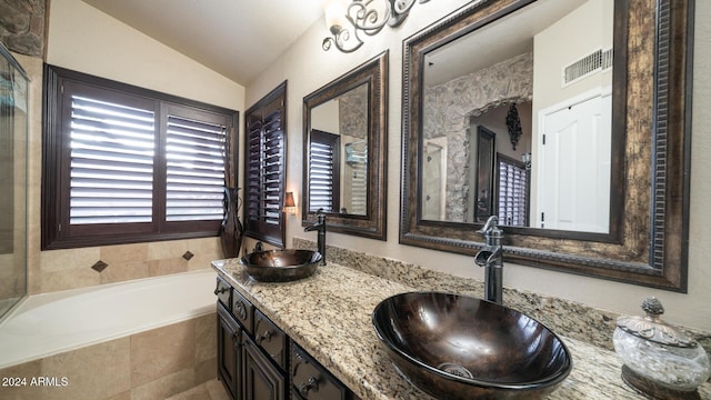 bathroom with vanity, tiled bath, and vaulted ceiling