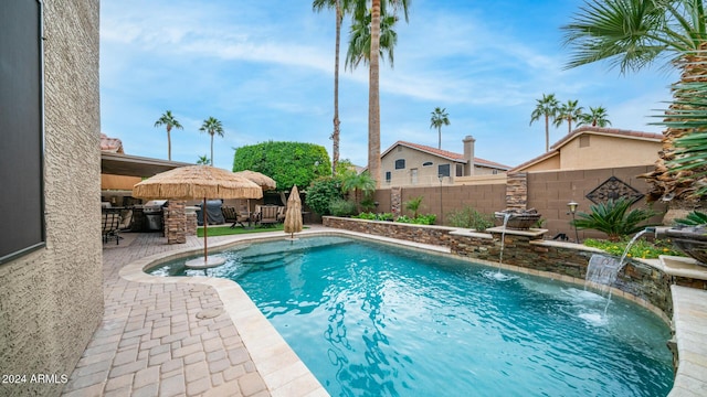 view of swimming pool featuring an outdoor kitchen, pool water feature, a bar, grilling area, and a patio