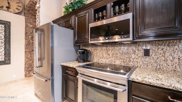 kitchen featuring tasteful backsplash, light stone counters, dark brown cabinets, and appliances with stainless steel finishes