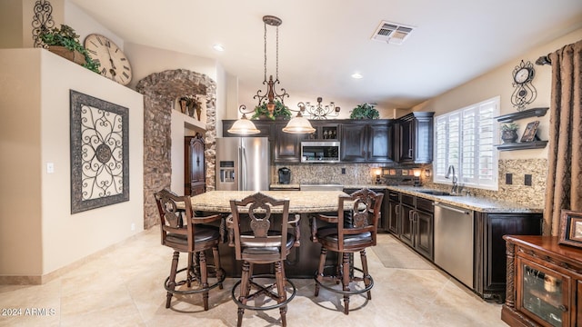 kitchen with sink, a center island, light stone counters, decorative light fixtures, and appliances with stainless steel finishes