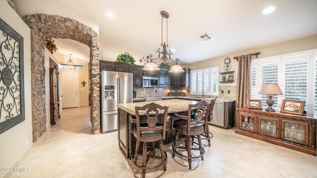 kitchen with light stone countertops, a center island, hanging light fixtures, a breakfast bar, and appliances with stainless steel finishes