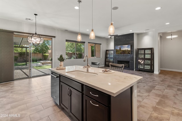 kitchen featuring sink, light stone counters, an island with sink, a high end fireplace, and pendant lighting