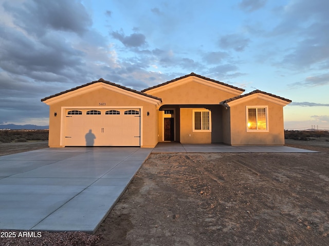 view of front of property featuring a tiled roof, an attached garage, driveway, and stucco siding