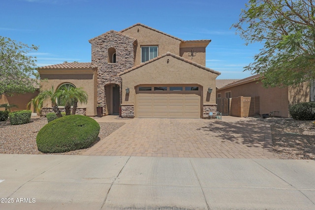 mediterranean / spanish house with a garage, stucco siding, stone siding, and decorative driveway