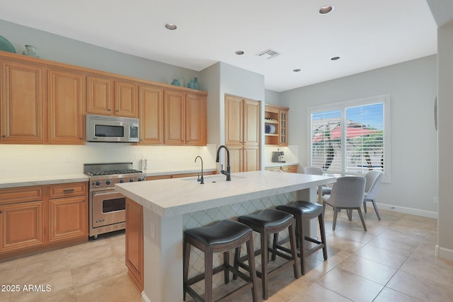 kitchen with stainless steel appliances, light countertops, a breakfast bar, tasteful backsplash, and a kitchen island with sink