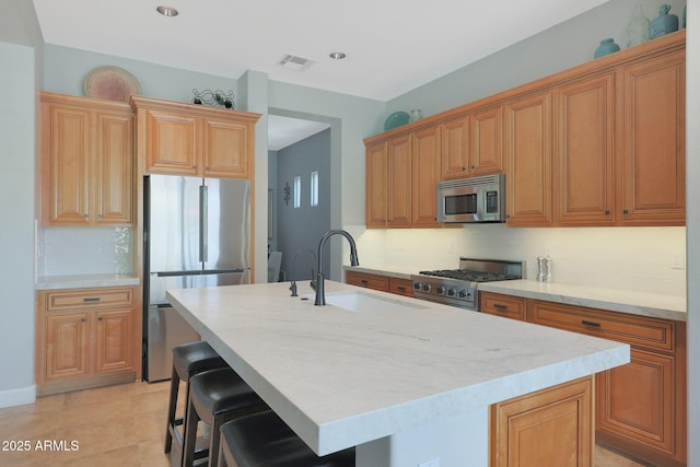 kitchen with stainless steel appliances, a sink, tasteful backsplash, a center island with sink, and a kitchen breakfast bar