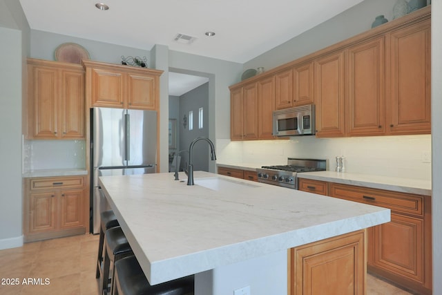 kitchen featuring appliances with stainless steel finishes, a sink, an island with sink, a kitchen bar, and tasteful backsplash