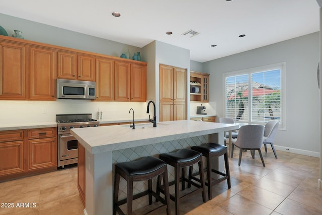 kitchen featuring stainless steel appliances, a sink, light countertops, a kitchen island with sink, and a breakfast bar