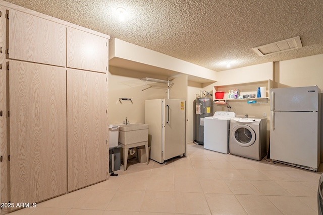 laundry room with light tile patterned floors, washing machine and dryer, electric water heater, and a textured ceiling