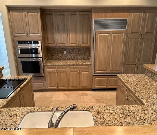 kitchen featuring sink, light stone countertops, paneled refrigerator, stainless steel double oven, and black electric cooktop