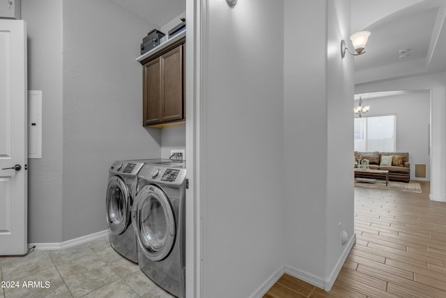 laundry area featuring a barn door, cabinets, a chandelier, washing machine and clothes dryer, and light hardwood / wood-style floors