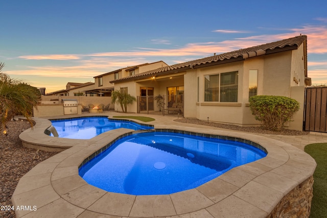 pool at dusk with a patio, an in ground hot tub, and grilling area