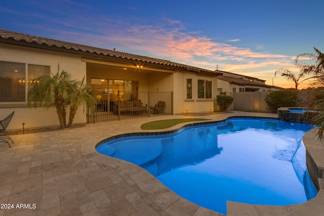 pool at dusk with a patio and an in ground hot tub