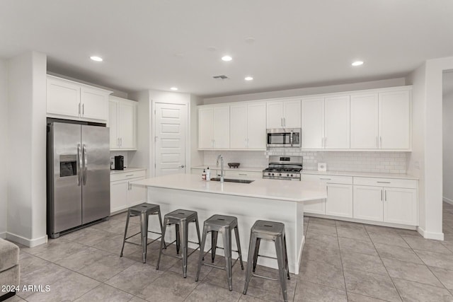 kitchen with sink, stainless steel appliances, an island with sink, a kitchen bar, and white cabinets