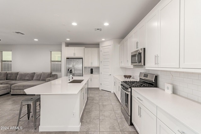 kitchen featuring decorative backsplash, appliances with stainless steel finishes, a kitchen island with sink, sink, and white cabinetry