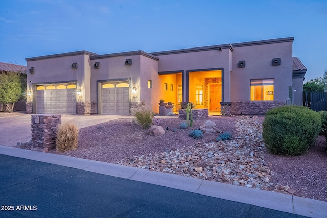 view of front facade with an attached garage, stone siding, driveway, and stucco siding