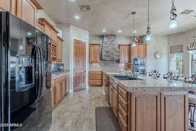 kitchen featuring visible vents, stainless steel microwave, black fridge, light wood-style floors, and a sink