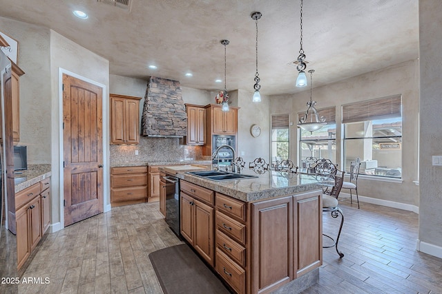 kitchen featuring light wood finished floors, a sink, a kitchen island with sink, and tasteful backsplash