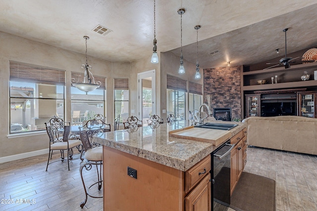 kitchen with a fireplace, a sink, visible vents, tile counters, and light wood finished floors