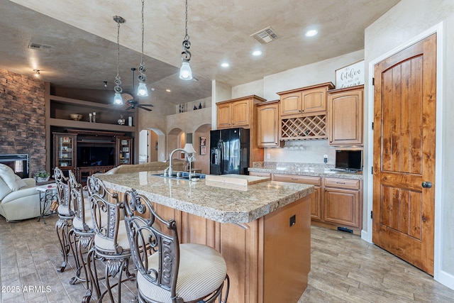 kitchen with arched walkways, open floor plan, black fridge with ice dispenser, and visible vents