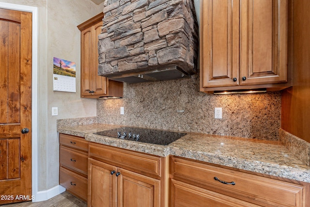 kitchen featuring baseboards, brown cabinetry, light stone counters, black electric cooktop, and backsplash