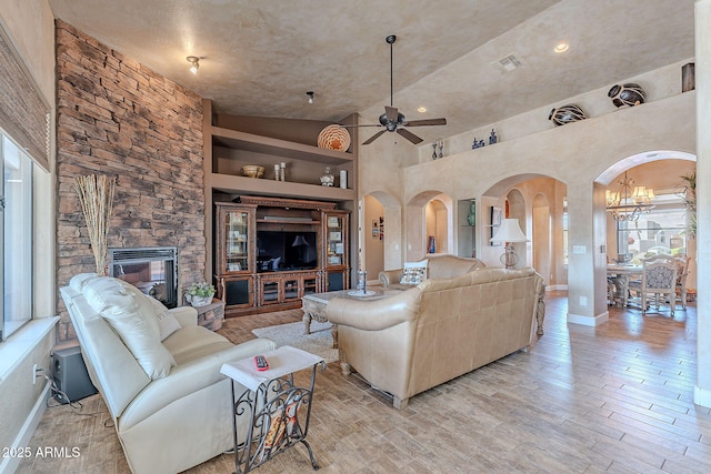 living area featuring light wood finished floors, visible vents, arched walkways, built in features, and ceiling fan with notable chandelier