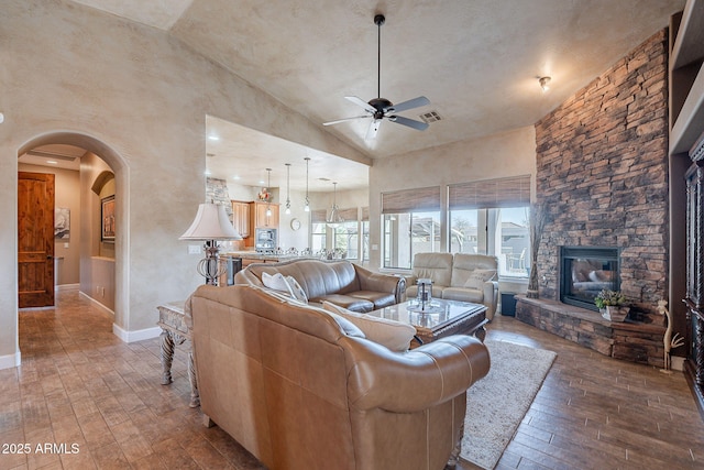 living area featuring arched walkways, wood-type flooring, visible vents, and a stone fireplace