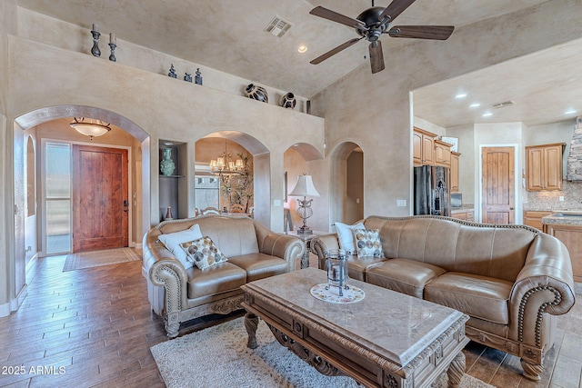 living room with arched walkways, high vaulted ceiling, wood finished floors, visible vents, and baseboards