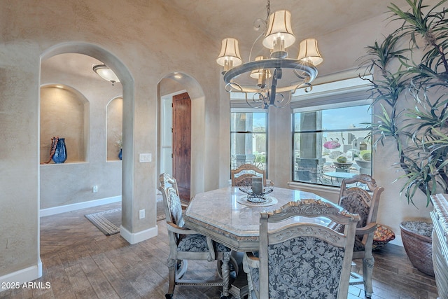 dining area with arched walkways, wood-type flooring, a textured wall, a chandelier, and baseboards