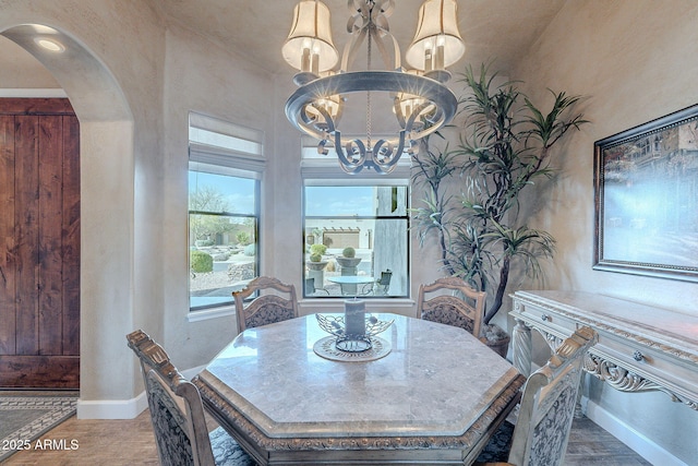 dining area featuring arched walkways, a notable chandelier, baseboards, and wood finished floors