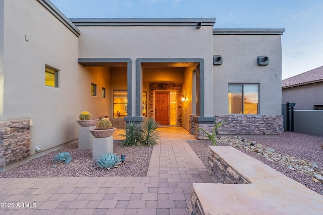 view of exterior entry featuring stone siding, fence, and stucco siding